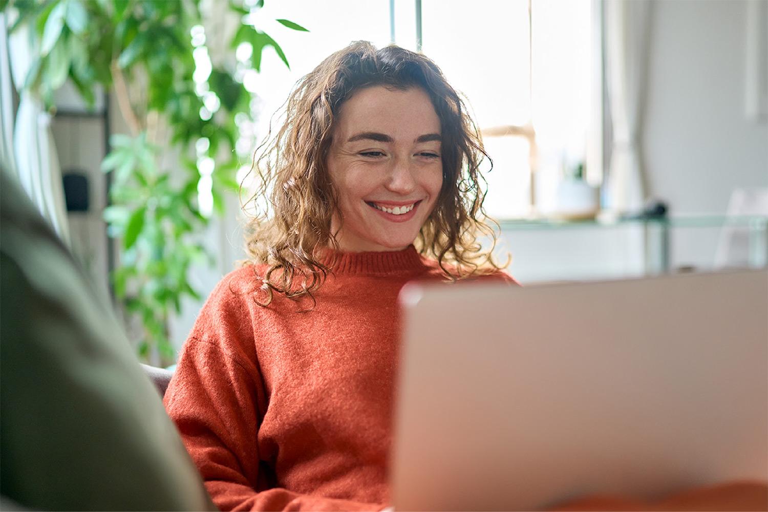 An image of a lady staring at a laptop and smiling.