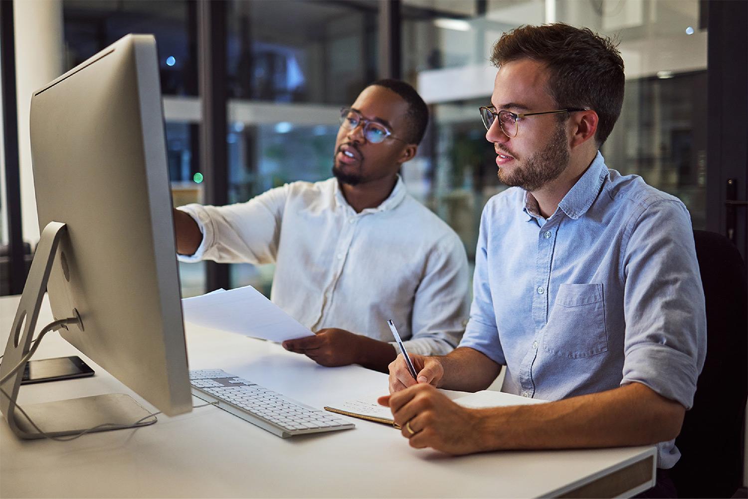 Two people sitting behind a laptop discussing something on the screen.
